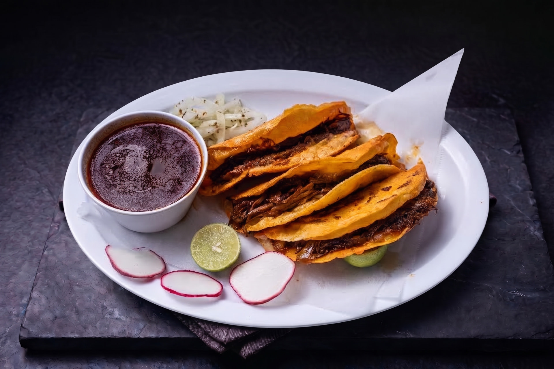 Quesabirria doradas servidas con consomé, limón y rábano